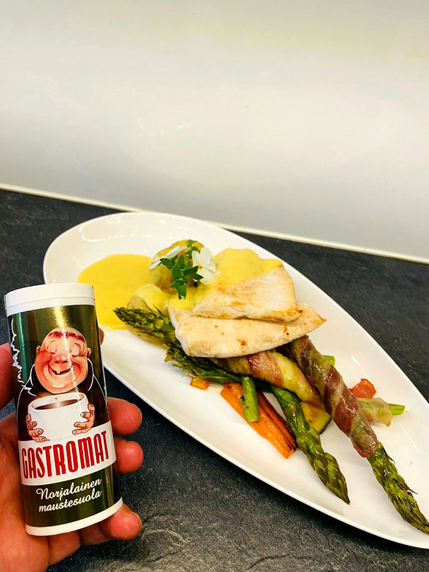 Kädessä Gastromat maustepurkki, valkoinen lautanen: kanaa, parsaa- ja kasviksia bearnaisekastikkeessa.